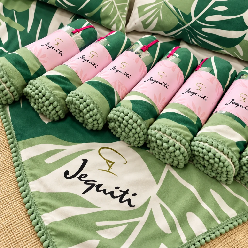 Canga personalizada com logo Jequiti, estampa folhagem verde com pompons, enroladas com cinta rosa para brinde corporativo